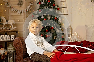 Cute blond toddler preschool boy, reading a book and opening present on Christmas on cozy home