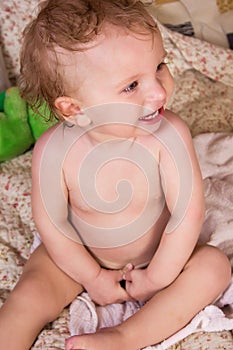 Cute blonde baby girl with beautiful blue eyes lying on bed with toy