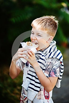 Cute blonde boy eating shrimp roll at fast food restaurant. Unhealthy meal for kids. Junk food.