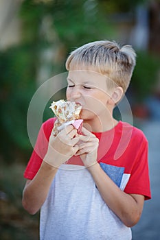 Cute blonde boy eating shrimp roll at fast food restaurant. Unhealthy meal for kids. Junk food.