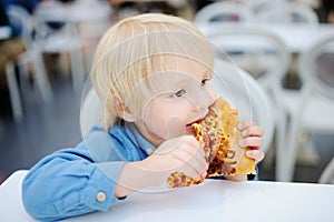 Cute blonde boy eating slice of pizza at fast food restaurant