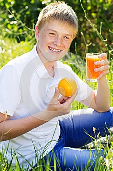 Cute blonde boy is holding glass with orange juice