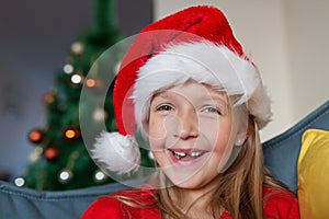 Cute blonde caucasian girl 7 years old sitting on couch near Christmas tree and writing letter to Santa Claus. Bedroom