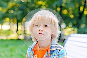 Cute blonde caucasian sad kid sitting on the bench at the park. Stress. emotion, depression