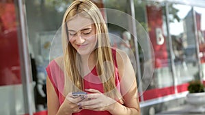 Cute blonde chatting with her friends using phone on the street