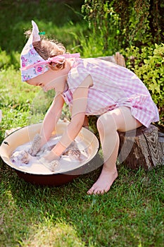 Cute blonde child girl plays toy wash in summer garden