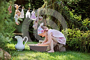 Cute blonde child girl plays toy wash in summer garden