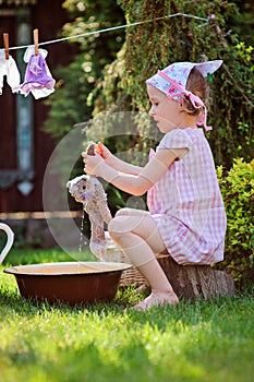 Cute blonde child girl plays toy wash in summer garden