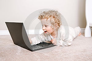 Cute blonde curly toddler baby boy working on laptop. Little kid child using technology. Early age education and development.