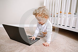 Cute blonde curly toddler baby boy working on laptop. Little kid child using technology. Early age education and development.