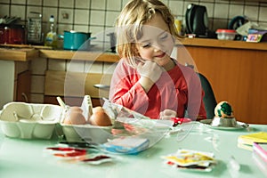 Cute blonde girl decorating Easter eggs at home.