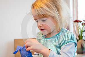 Cute blonde girl playing with medical rubber gloves at home.