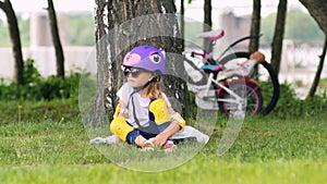 Cute blonde girl sitting under the tree wearing bicycle helmet