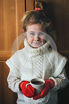 Cute blonde little girl holding hot steaming tea cup close up photo