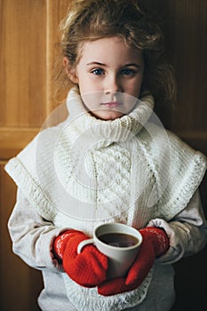 Cute blonde little girl holding hot steaming tea cup close up photo