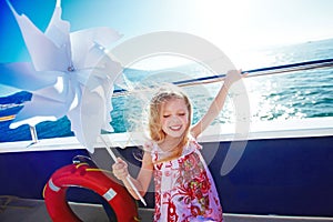 Cute blonde long haired six years old girl is playing with pinwheel on cruise ship deck