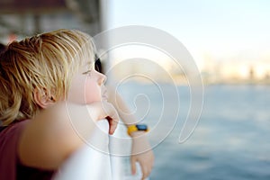 Cute blonde preteen boy is traveling by boat or ferry on the sea. Family vacations on ocean or sea. Summer leisure for families