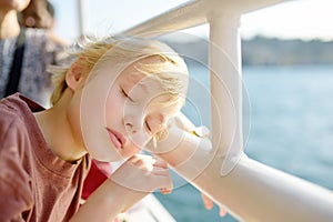 Cute blonde preteen boy is traveling by boat or ferry on the sea. Family vacations on ocean or sea. Summer leisure for families