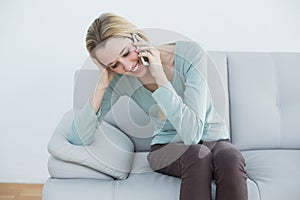 Cute blonde woman phoning happily sitting on couch
