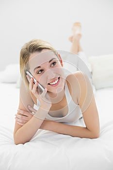 Cute blonde woman phoning with her smartphone lying on her bed at home