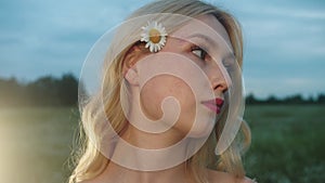 Cute blonde young woman puts a chamomile on her ear