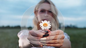 Cute blonde young woman sniffs a daisy and holds it into the camera