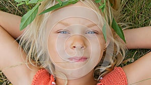 Cute blue-eyed blonde seven-year-old girl with a dirty face. Child is lying on the grass with her hands behind her head
