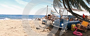 Cute blue retro car with summer accessories and palm tree on beautiful tropical sand beach. Summer vacation concept.