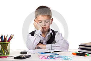 Cute bored pupil sitting with lowered eyes at the desk with hand under the chin surrounded with stationery
