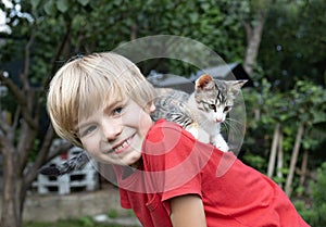 cute boy of 6-7 years old plays with his beloved kitten, which sits on his back