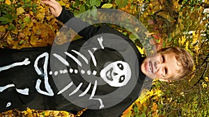 A cute boy of 7-8 years old in a costume with the image of a skeleton rejoices during Halloween