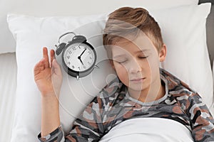 Cute boy with alarm clock sleeping in bed