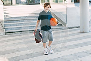 A cute boy with a backpack in one hand and a basketball in the other. The boy in shape in a hurry for a workout but basketball.