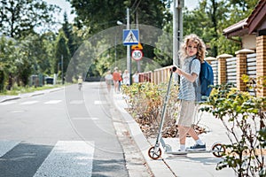 Boy with a backpack and scooter is standing in front of a pedestrian crossing on the street