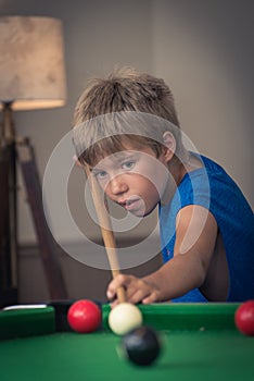 Cute boy in blue t shirt plays billiard or pool in club. Young Kid learns to play snooker. Boy with billiard cue strikes the ball