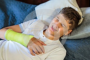 Cute boy with broken hand hearts. Close up young handsome Teenage with elbow plaster at home