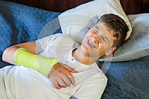 Cute boy with broken hand hearts. Close up young handsome Teenage with elbow plaster at home