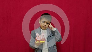 Cute boy in business suit holding piggy bank and getting frustrated as it is empty. Savings investment and recession