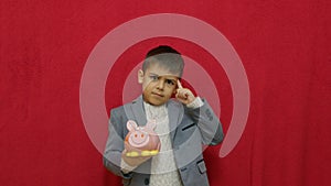 Cute boy in business suit holding piggy bank and getting an idea how to earn more money. Steals the piggy bank.