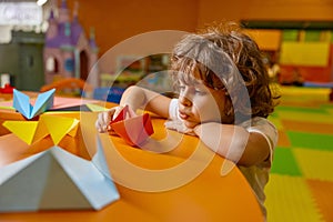 Cute boy child playing handmade origami paper boat at childcare center
