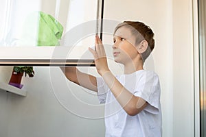 A cute boy is cleaning, washing an open window on the balcony