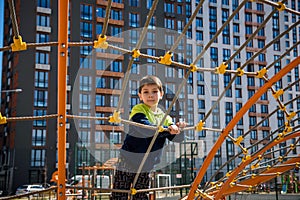 Cute boy is climbing on the playground in the schoolyard. He has a very happy face and enjoy this adventure sports alone outdoor.
