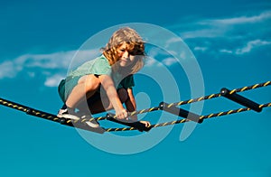 Cute boy climbs up the ladder on the playground. Child climbs up the ladder against the blue sky. Beautiful smiling cute