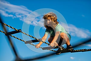 Cute boy climbs up the ladder on the playground. Child climbs up the ladder against the blue sky. Young boy exercise out