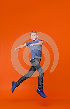 Cute boy dancing, jumping in air on orange backgrouns