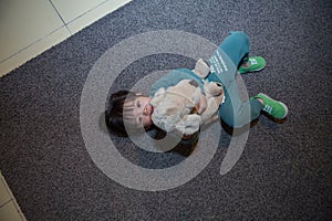 cute boy in a dark green suit is lying on the gray carpet and playing