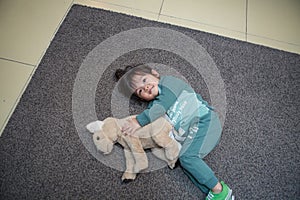 cute boy in a dark green suit is lying on the gray carpet and playing