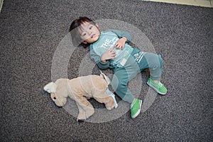 cute boy in a dark green suit is lying on the gray carpet and playing