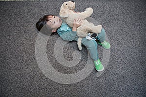 cute boy in a dark green suit is lying on the gray carpet and playing