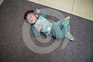 cute boy in a dark green suit is lying on the gray carpet and playing